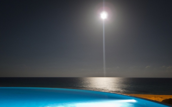 Der Mond leuchtet über dem Meer, davor ein hellblauer Pool
